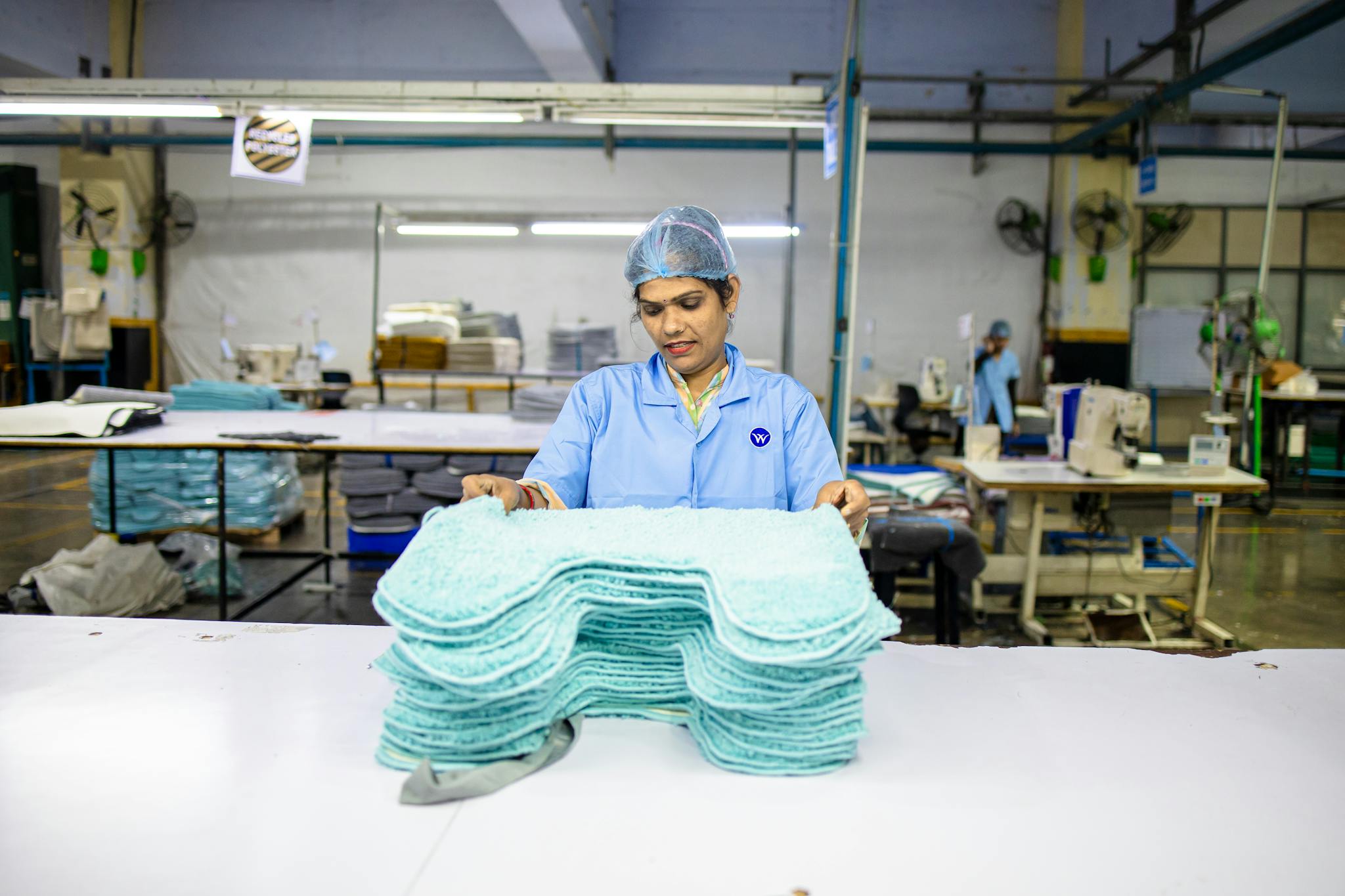 A textile worker sorts blue fabric pieces in a factory setting, showcasing the industrial work environment.