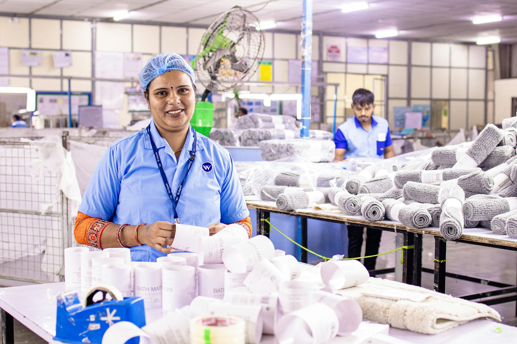 Confident female factory worker inspects and organizes textile products at a bustling industrial facility.
