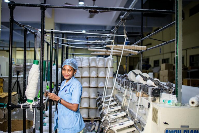 Female textile worker operates machinery in an industrial factory setting.