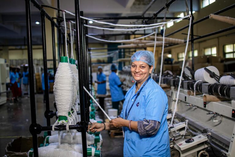 Smiling textile worker operating machinery in an industrial factory environment.