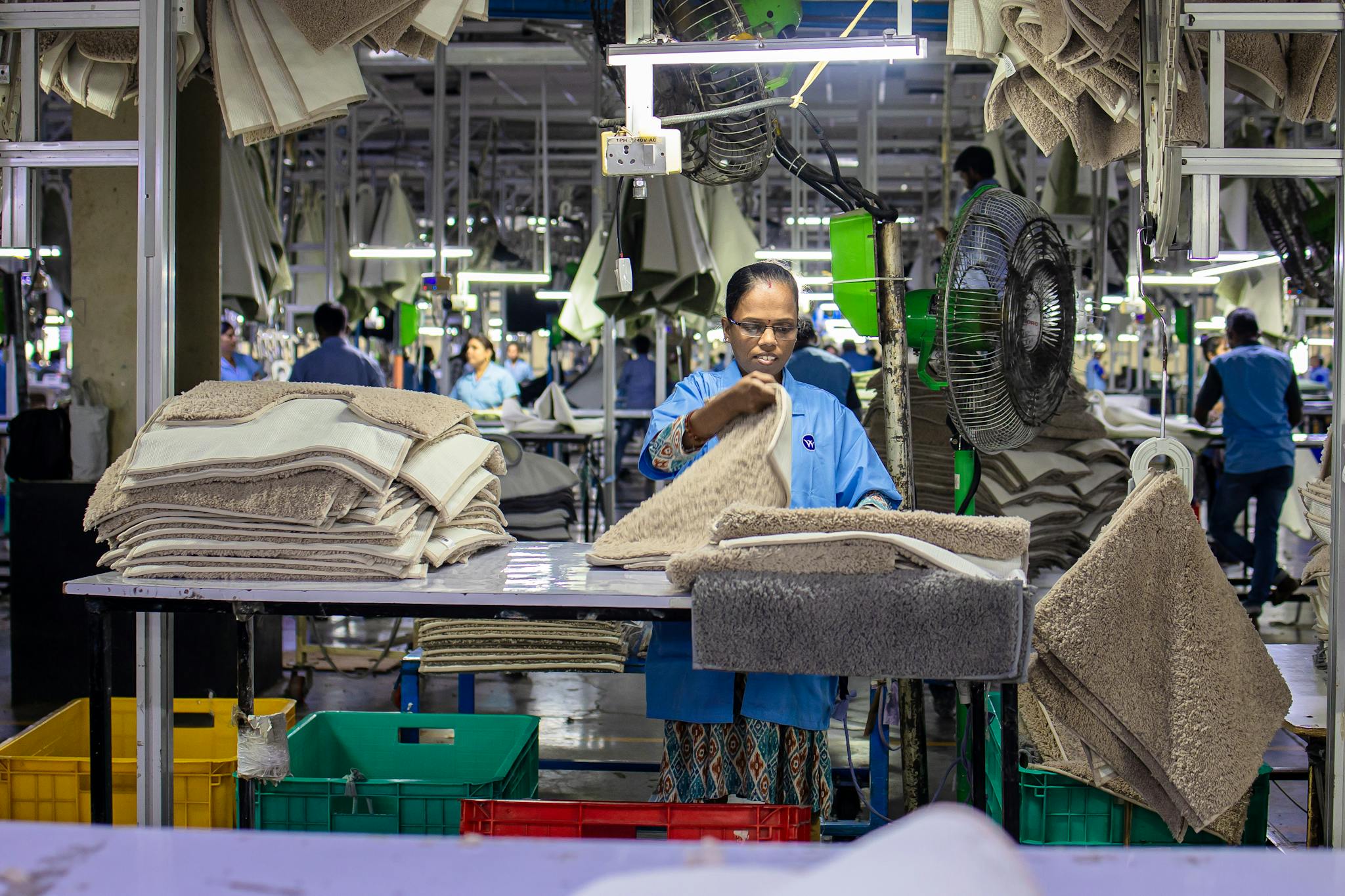 Woman organizing textile products in a bustling factory environment.